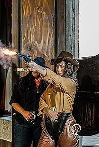 Woman dressed as cowboy, shooting a gun.